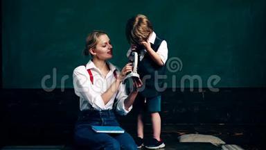 一个带着小男孩的女人看着绿色瞳孔`s板背景上的显微镜。 课堂教师